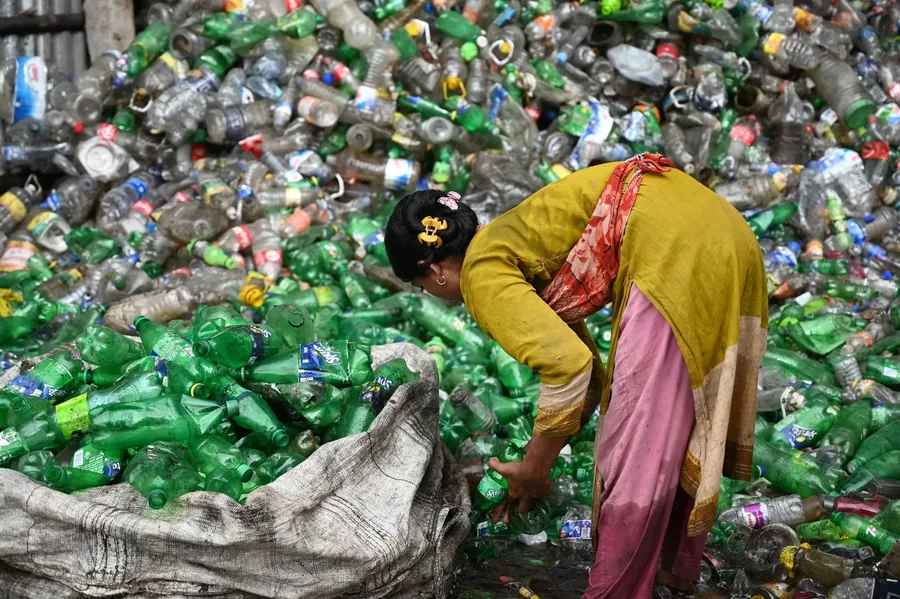 A woman sorting a mountain of plastic by hand, the work nobody counts.