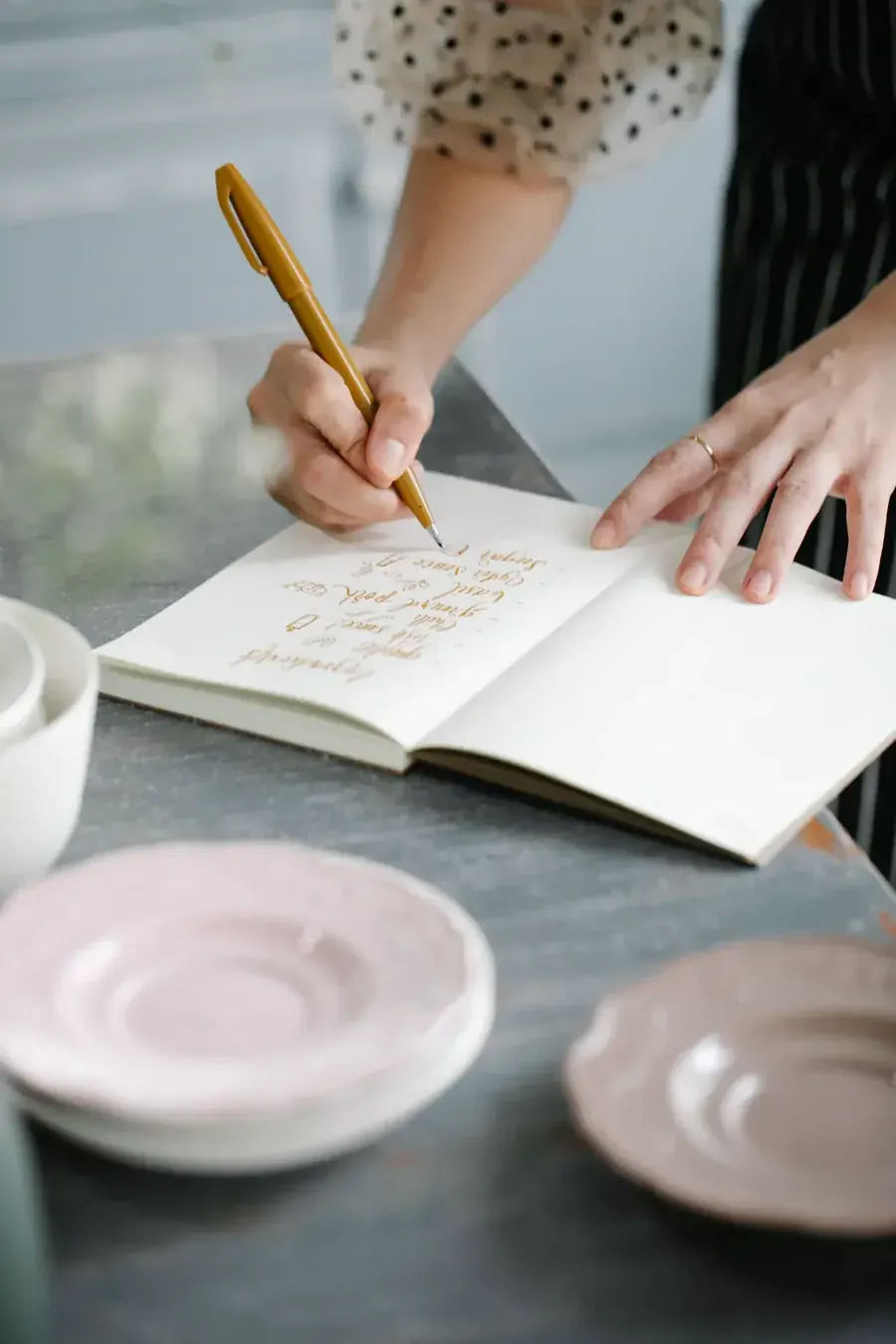 A woman writing by hand beside a cooling cup, saying it to the page instead.