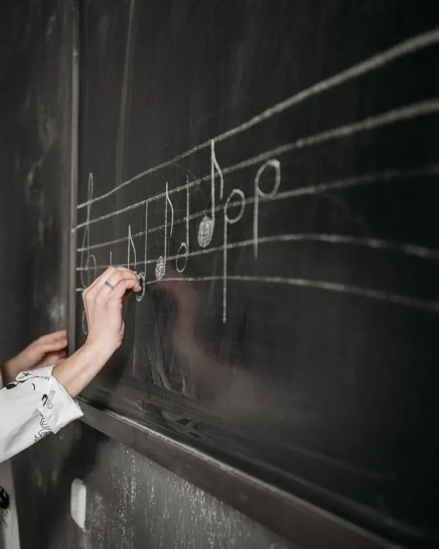 A hand writing notes on a blackboard where everyone can see the working out.