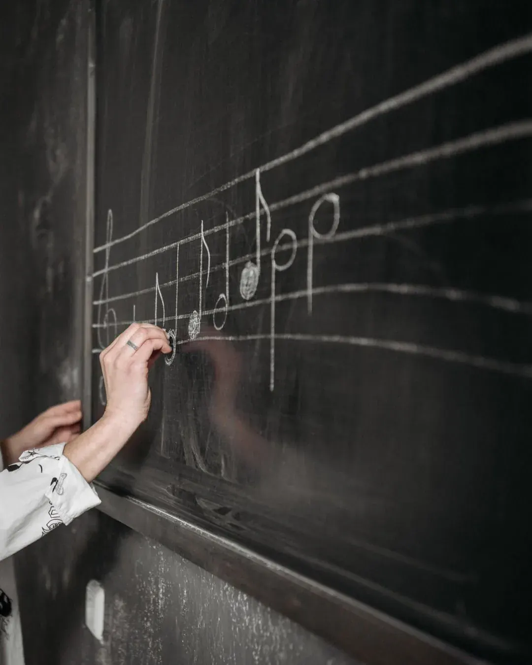 A hand writing notes on a blackboard where everyone can see the working out.