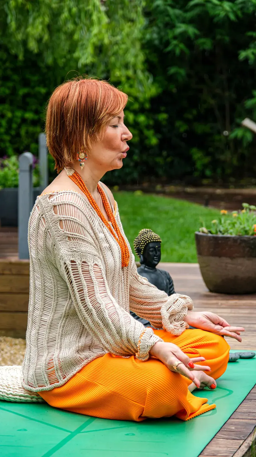 A woman sitting quietly outdoors, a softness that still knows exactly where it is.