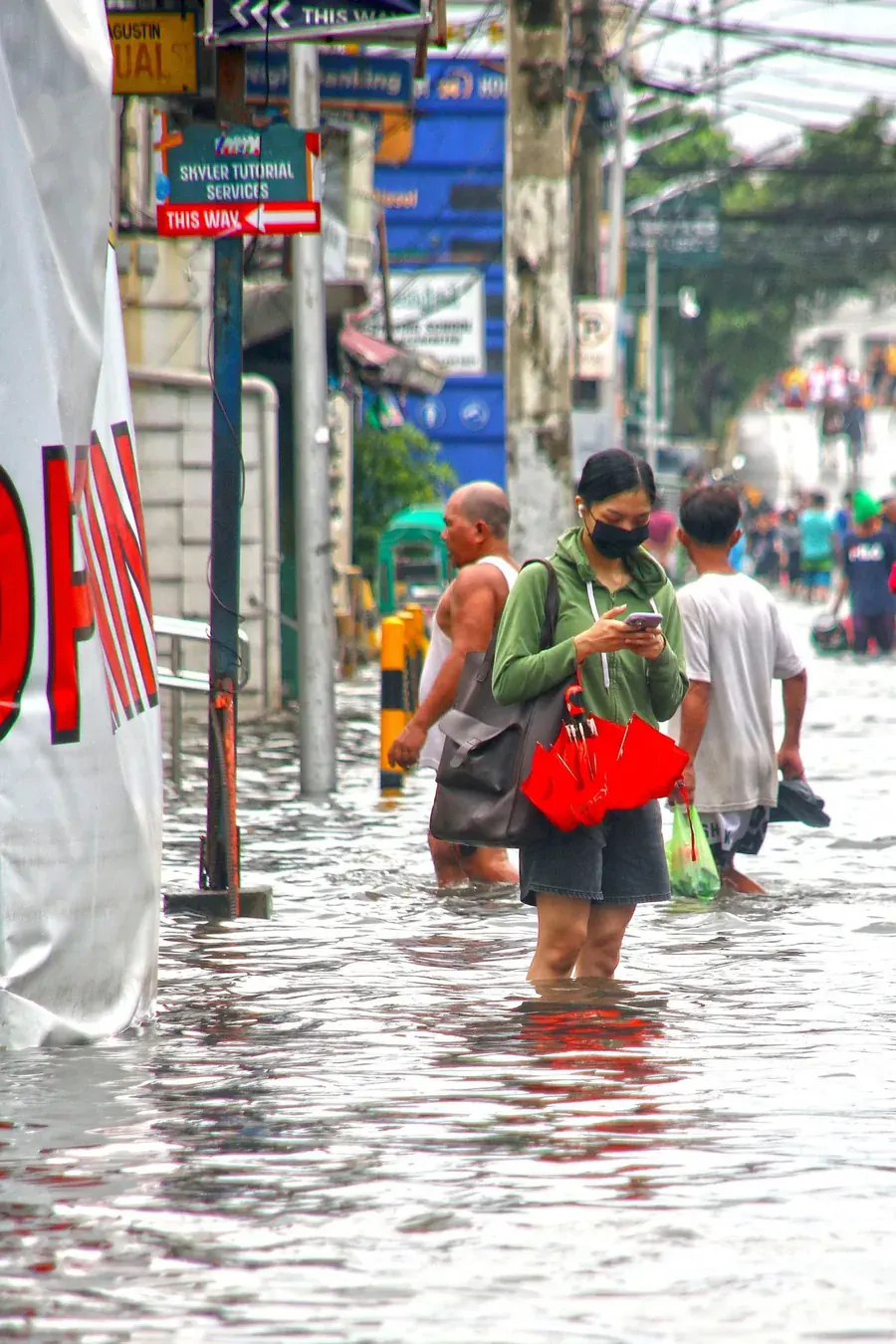 People wading home through a flooded street, the cost arriving somewhere else.