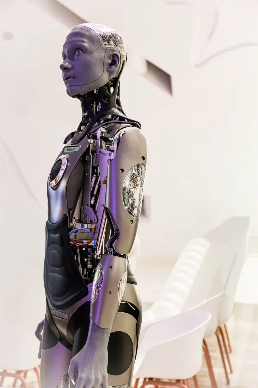 A humanoid robot standing in an empty room, its almost-human face quietly doing the work of persuasion.