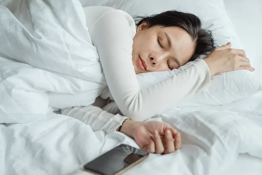 A woman asleep with her phone beside her, the night measured while she rests.