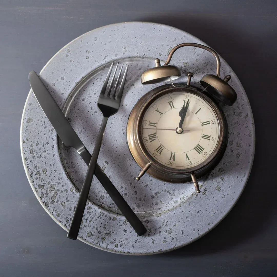 An empty plate with a clock where the meal should be, hunger keeping to the hour.