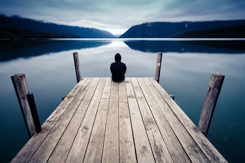 A person sitting at the end of a dock, continuing with nobody watching.